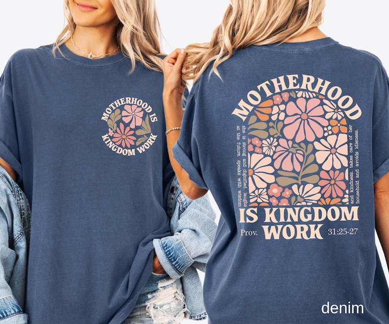 May include: A denim blue t-shirt featuring the text "MOTHERHOOD IS KINGDOM WORK" and a floral design on the front. The back of the shirt displays the same text and floral design, along with a quote from Proverbs 31:25-27.