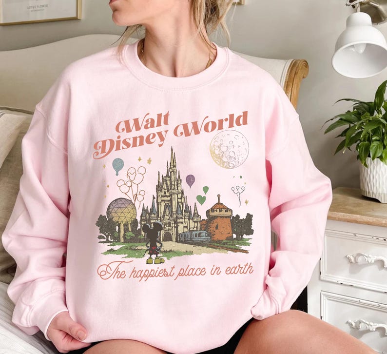 May include: Pink sweatshirt with a graphic of Cinderella's castle, Mickey Mouse, and the text "Walt Disney World" and "The happiest place in earth". The design includes balloons, a train, and a moon.