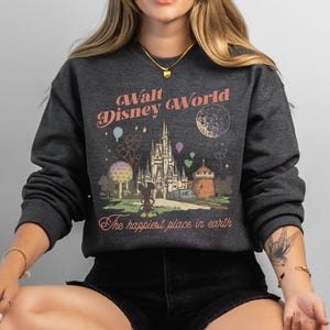 May include: Dark gray sweatshirt with a vintage-style graphic of Walt Disney World. The design includes a castle, Mickey Mouse, and the text "The happiest place in earth."
