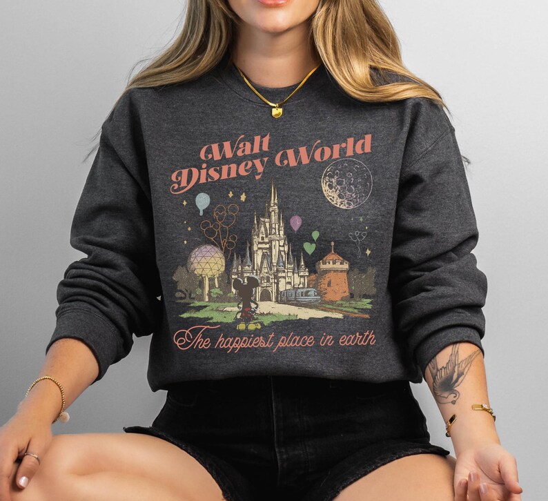May include: Dark gray sweatshirt with a vintage-style graphic of Walt Disney World. The design includes a castle, Mickey Mouse, and the text "The happiest place in earth."