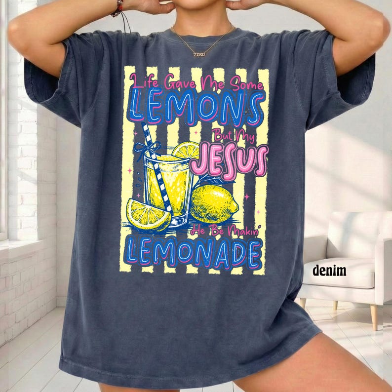 May include: Denim blue t-shirt with a graphic of a glass of lemonade, lemons, and the text "Life Gave Me Some Lemons But My Jesus He Be Makin' Lemonade". The design has yellow and white stripes.