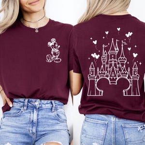 Puede incluir: Camiseta burdeos con un boceto blanco de Mickey Mouse en la parte delantera y un dise&ntilde;o de castillo en la parte trasera. El dise&ntilde;o del castillo incluye orejas de Mickey Mouse en la base, globos y estrellas. La camiseta es de material suave.