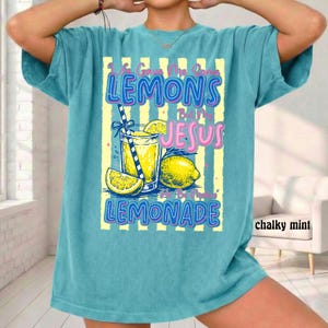 May include: A turquoise t-shirt with a graphic of a lemonade drink, lemons, and the text "Life Gave Me Lemons But I Made Lemonade". The design includes yellow and blue accents.