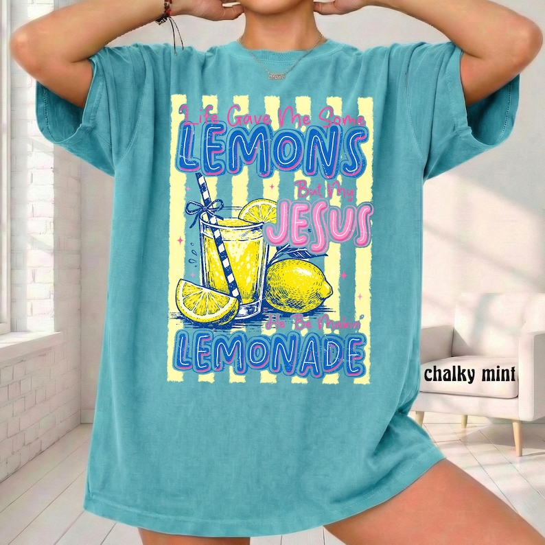 May include: A turquoise t-shirt with a graphic of a lemonade drink, lemons, and the text "Life Gave Me Lemons But I Made Lemonade". The design includes yellow and blue accents.