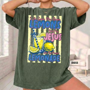 May include: Moss green t-shirt with a graphic of a lemonade drink, lemons, and the text "Life Gave Me Some Lemons But My Jesus He Be Makin' Lemonade". The design features yellow, blue, and pink colors.