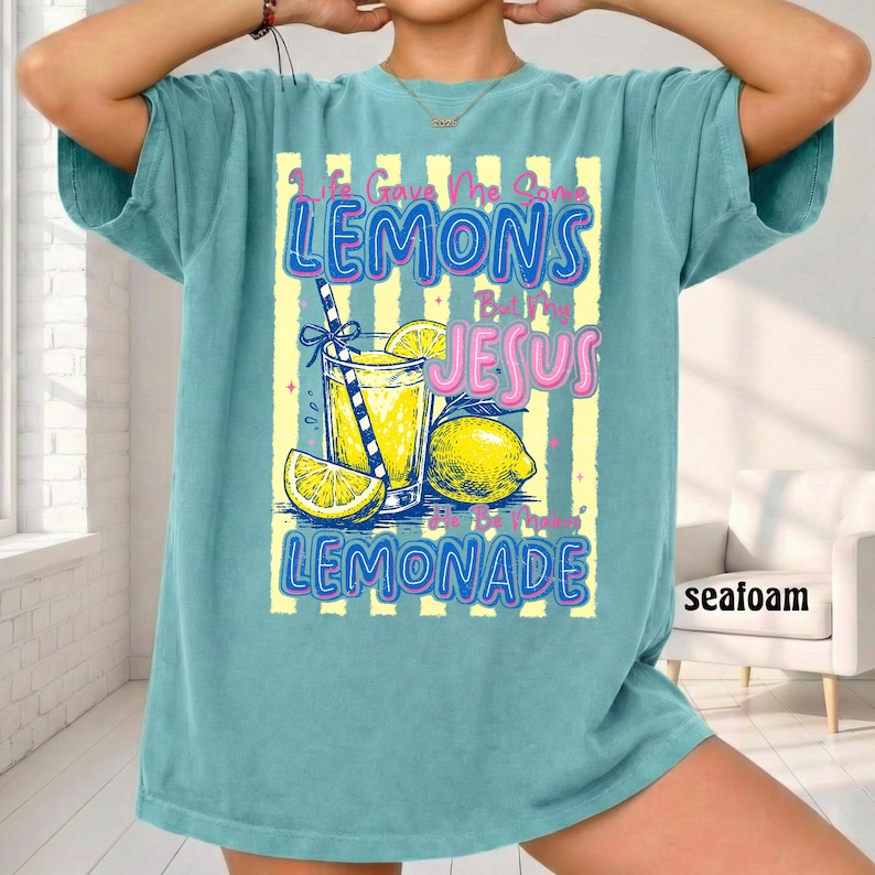 May include: Seafoam green t-shirt with a graphic of a glass of lemonade, lemons, and the text "Life Gave Me Lemons But My Jesus Made Lemonade." The design has yellow and blue accents.