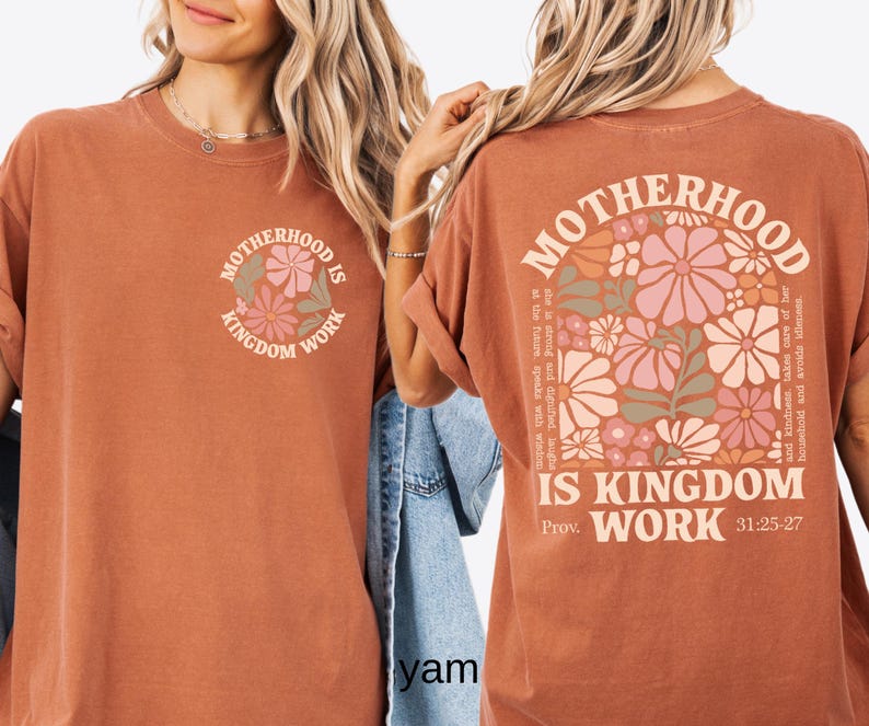 May include: A terracotta-coloured t-shirt with the words "MOTHERHOOD IS KINGDOM WORK" and a floral design. The back of the shirt has the same text and a larger floral arrangement with text from Proverbs 31:25-27.