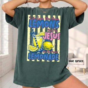 May include: Dark teal t-shirt with a graphic of a lemonade drink, lemons, and the text "Life Gave Me Some Lemons But My Jesus He Be Makin' Lemonade". The design is on a yellow and white striped background.