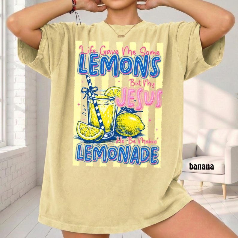 May include: A light yellow t-shirt with the text "Life Gave Me Some Lemons But My Jesus He Be Makin' Lemonade." The graphic includes a glass of lemonade, lemons, and a straw.