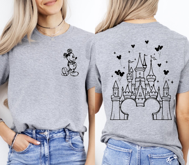 Puede incluir: Una camiseta gris con un dibujo en blanco y negro de Mickey Mouse en la parte delantera y un dise&ntilde;o de castillo en la parte trasera. El dise&ntilde;o del castillo incluye orejas y globos de Mickey Mouse.