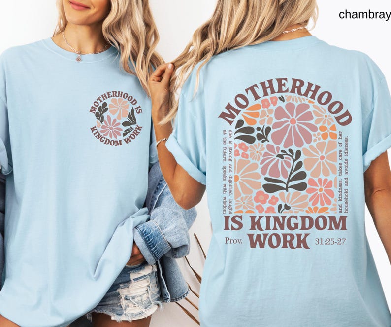 May include: Pale blue t-shirt with the text "MOTHERHOOD IS KINGDOM WORK" and a floral design. The back of the shirt features the same text and a larger floral arrangement. The shirt has rolled-up sleeves.