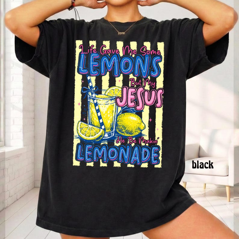 May include: Black t-shirt with a colorful graphic of a lemonade drink, lemons, and the text "Life Gave Me Some Lemons But My Jesus He Be Makin' Lemonade." The design includes yellow and blue accents.