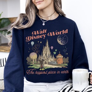 May include: Navy blue sweatshirt featuring a vintage-style graphic of Cinderella's castle, Mickey Mouse, and the text "Walt Disney World" and "The happiest place in earth". The design includes balloons and a crescent moon.