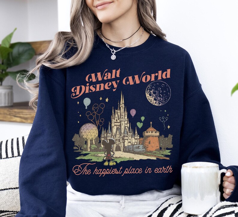 May include: Navy blue sweatshirt featuring a vintage-style graphic of Cinderella's castle, Mickey Mouse, and the text "Walt Disney World" and "The happiest place in earth". The design includes balloons and a crescent moon.