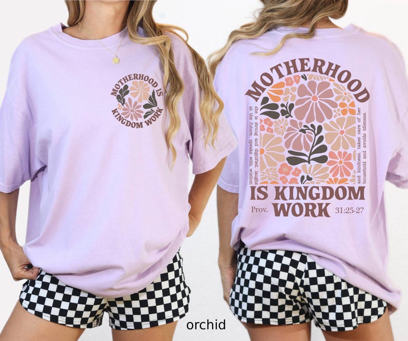 May include: Lilac t-shirt featuring the text "MOTHERHOOD IS KINGDOM WORK" and a floral design on the front and back. The back also includes the Bible verse Proverbs 31:25-27. The model is wearing black and white checkered shorts.