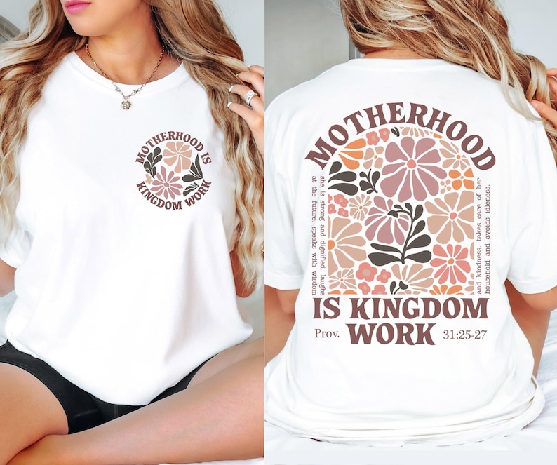 May include: White t-shirt featuring the text "MOTHERHOOD IS KINGDOM WORK" in a circular design on the front and back. The back design includes a floral arrangement in pink, peach, and brown, with a quote from Proverbs 31:25-27.