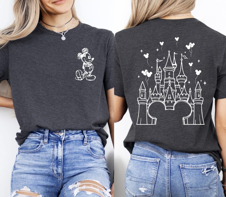 Puede incluir: Camiseta gris oscuro con un boceto blanco de Mickey Mouse en la parte delantera y un dise&ntilde;o de castillo blanco en la parte trasera. El dise&ntilde;o del castillo incluye orejas de Mickey Mouse, globos y estrellas. La camiseta se combina con vaqueros azules.