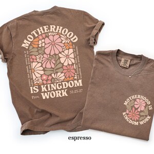 May include: Two espresso-coloured t-shirts. One features a floral design and the text "MOTHERHOOD IS KINGDOM WORK" on the back, with additional text from Proverbs 31:25-27. The other shirt has the same design on the front.