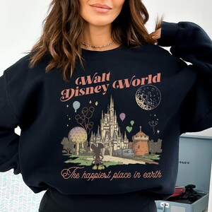 May include: Black sweatshirt featuring a vintage-style graphic of Walt Disney World. The design includes the castle, Mickey Mouse, balloons, and the text "The happiest place in earth". The text "Walt Disney World" is arched across the top.