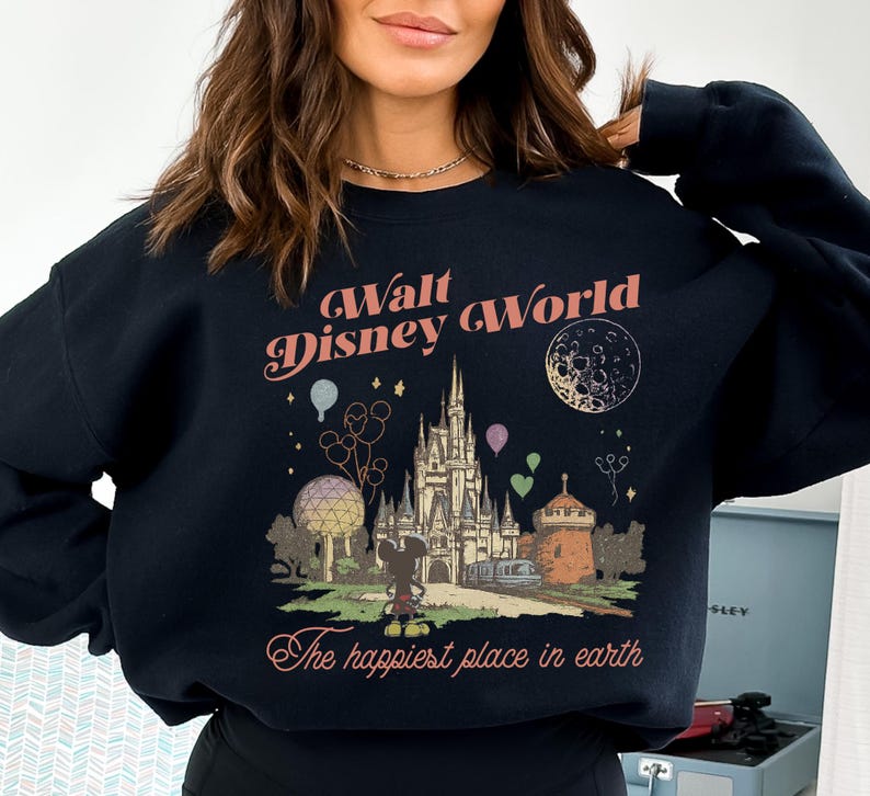 May include: Black sweatshirt featuring a vintage-style graphic of Walt Disney World. The design includes the castle, Mickey Mouse, balloons, and the text "The happiest place in earth". The text "Walt Disney World" is arched across the top.