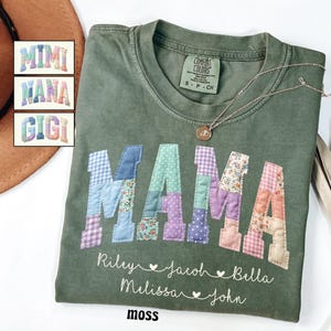 May include: A moss green t-shirt with the word "MAMA" in patchwork letters. Below the word "MAMA" are the names Riley, Jacob, Bella, Melissa, and John. A gold necklace with a pendant is on the shirt. The word "moss" is at the bottom.