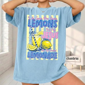 May include: Light blue t-shirt with a graphic of a lemonade drink, lemons, and the text "Life Gave Me Some Lemons But My Jesus He Be Makin' Lemonade." The shirt has short sleeves and a relaxed fit.
