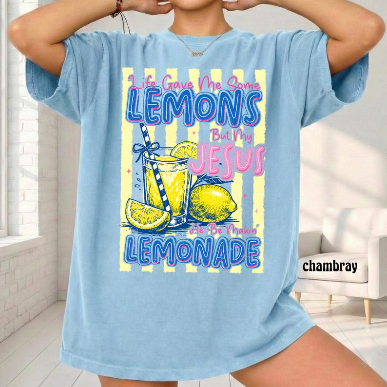 May include: Light blue t-shirt with a graphic of a lemonade drink, lemons, and the text "Life Gave Me Some Lemons But My Jesus He Be Makin' Lemonade." The shirt has short sleeves and a relaxed fit.