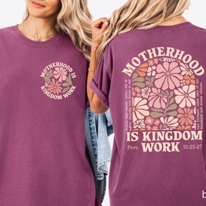 May include: Berry-coloured t-shirt with the text "Motherhood is Kingdom Work" and a floral design on the front and back. The back of the shirt features a larger floral design and the Bible verse Proverbs 31:25-27.