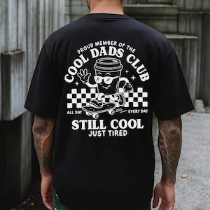 Pu&ograve; includere: T-shirt nero con grafica bianca di una tazza di caff&egrave; con occhiali da sole e che fa skateboard. Il testo recita "PROUD MEMBER OF THE COOL DADS CLUB" e "STILL COOL JUST TIRED".