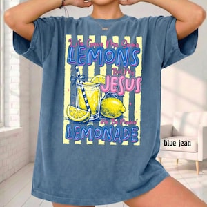 May include: A blue jean-colored t-shirt with a graphic of a lemonade drink, lemons, and the text "Life Gave Me Some Lemons But My Jesus He Be Makin' Lemonade" in pink and blue. The shirt has short sleeves.