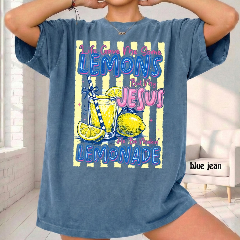 May include: A blue jean-colored t-shirt with a graphic of a lemonade drink, lemons, and the text "Life Gave Me Some Lemons But My Jesus He Be Makin' Lemonade" in pink and blue. The shirt has short sleeves.