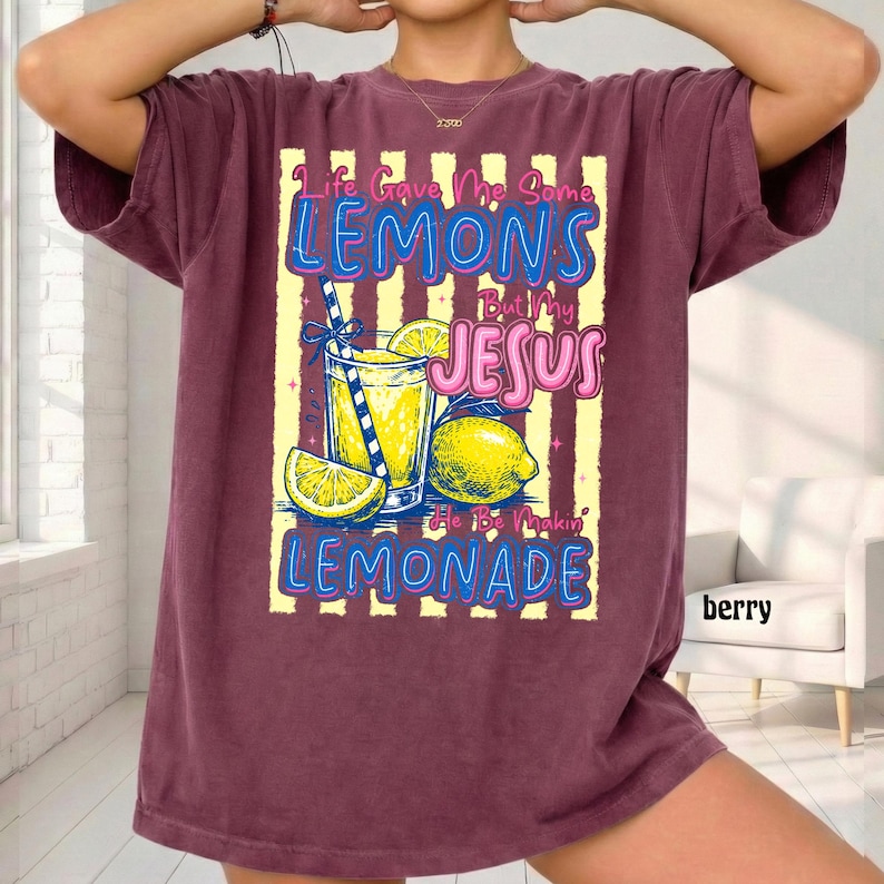 May include: Berry-colored t-shirt with a graphic of a lemonade drink, lemons, and the text "Life Gave Me Some Lemons But My Jesus He Be Makin' Lemonade." The shirt has a relaxed fit.