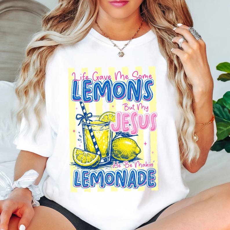 May include: White t-shirt with a colorful graphic that reads "Life Gave Me Some Lemons But My Jesus He Be Makin' Lemonade." The design includes a glass of lemonade, lemons, and a striped straw. The text is in blue and pink.
