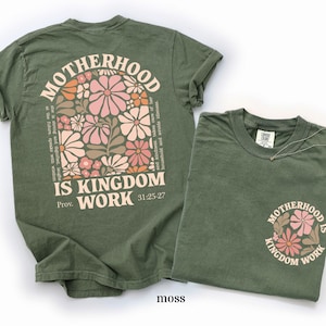 May include: Two moss-green t-shirts. One features the text "MOTHERHOOD IS KINGDOM WORK" with floral graphics. The other shirt has the same text and floral design on the front pocket. The text "Prov. 31:25-27" is also visible.