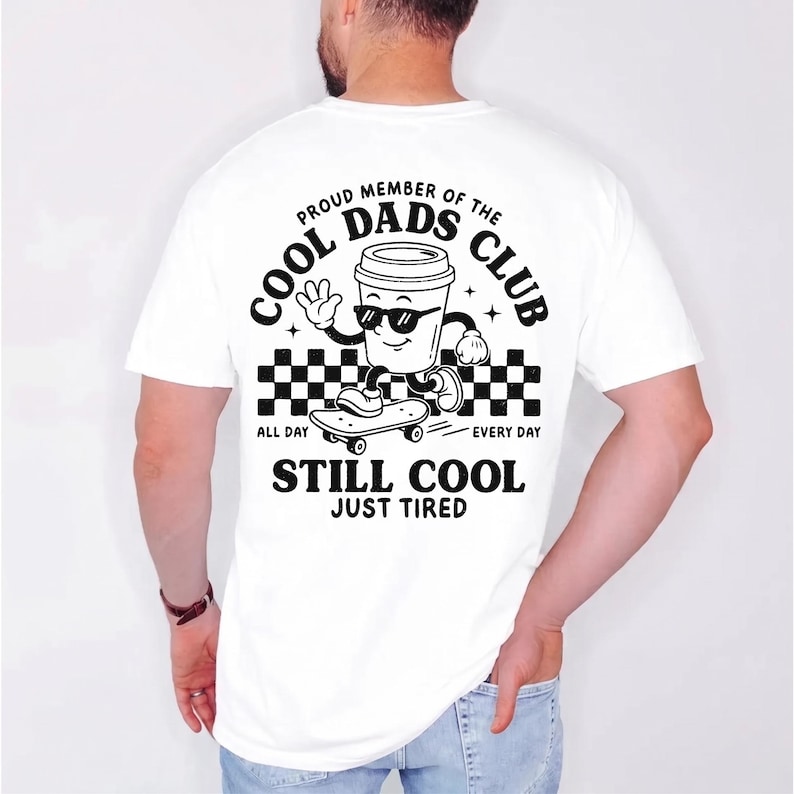 Pu&ograve; includere: T-shirt bianco con grafica nera di una tazza di caff&egrave; con occhiali da sole su uno skateboard. Il testo recita "PROUD MEMBER OF THE COOL DADS CLUB" e "STILL COOL JUST TIRED".