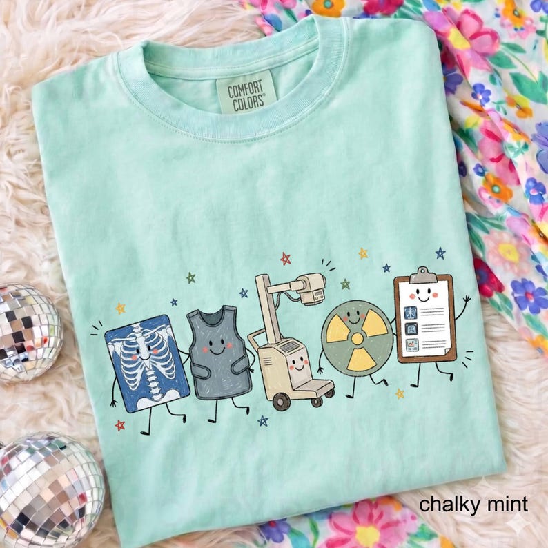 May include: A light mint green t-shirt with a Comfort Colors label at the neck. The graphic features five cartoon characters: an X-ray of a rib cage, a lead apron, an X-ray machine, a radiation symbol, and a clipboard, all with smiling faces.