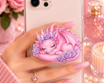 May include: A light pink smartphone case featuring a circular grip attachment with a detailed illustration of a sleeping baby dragon. The dragon is pink with purple accents, wearing a bow and surrounded by purple roses on a clear circular base.