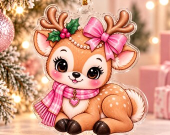 May include: A clear acrylic ornament shaped like a cartoon fawn with large brown eyes, wearing a pink plaid scarf with a heart charm and a pink bow on its antlers. The fawn features white spots, holly leaves with red berries, and a gold hanging cord.
