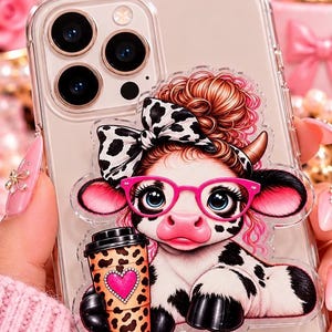 May include: A clear smartphone case featuring a decorative acrylic attachment of a cartoon cow with a messy bun, a black and white cow-print bow, and bright pink glasses. The cow holds a leopard-print coffee cup with a pink heart design.