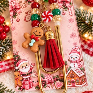 May include: A gold-toned metal paperclip bookmark featuring a gingerbread man charm with a red bow, a red suede tassel, and a strand of red, green, and gold crackle beads accented by a small round peppermint candy charm.
