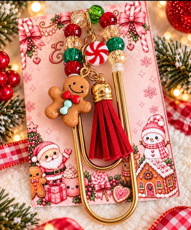 May include: A gold-toned metal paperclip bookmark featuring a gingerbread man charm with a red bow, a red suede tassel, and a strand of red, green, and gold crackle beads accented by a small round peppermint candy charm.