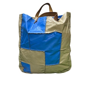 May include: A patchwork tote bag in tan and blue. It has a leather handle and a rectangular shape. The bag is made of a durable material and is suitable for carrying various items. The bag's dimensions are approximately 30 cm x 30 cm.