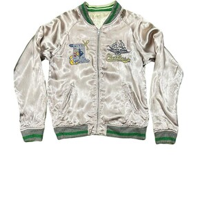 May include: A light silver satin bomber jacket with green and gray striped trim. The jacket features embroidered patches including a ship and the word "Cutlass". The jacket has a zipper closure and two front pockets.