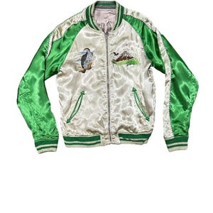 May include: Cream-colored satin bomber jacket with green sleeves and trim. Features embroidered images of a bird and a mountain. The jacket has a zipper closure and two front pockets.