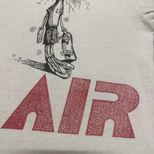 May include: White t-shirt with a cartoon skater graphic in black and white, and the word "AIR" in large red letters. The skater is drawn in a whimsical style, holding a skateboard.