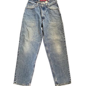 May include: Light blue denim jeans with a loose fit. The jeans feature a classic five-pocket design, a button and zip closure, and the word "LOOSE" printed on the red tag. The jeans are pre-worn with faded areas.