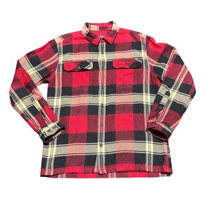 May include: A red, black, and tan plaid flannel shirt with two chest pockets. The long-sleeved shirt has a button-down front and cuffs. The fabric has a classic lumberjack style pattern.