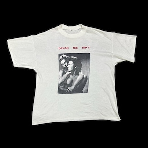 May include: White t-shirt with a black and white graphic of two people embracing. The text "DESIGN FOR SKP'T" is printed in red above the graphic. The shirt has short sleeves and a crew neck.