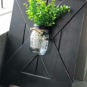 Peut inclure: Une pancarte en bois noir avec un motif en X d&eacute;coratif. Un bocal en verre avec une plante verte est fix&eacute; &agrave; la pancarte.