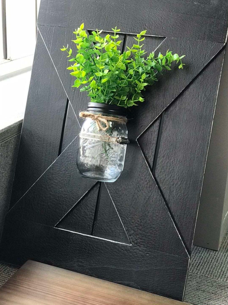 Peut inclure: Une pancarte en bois noir avec un motif en X d&eacute;coratif. Un bocal en verre avec une plante verte est fix&eacute; &agrave; la pancarte.